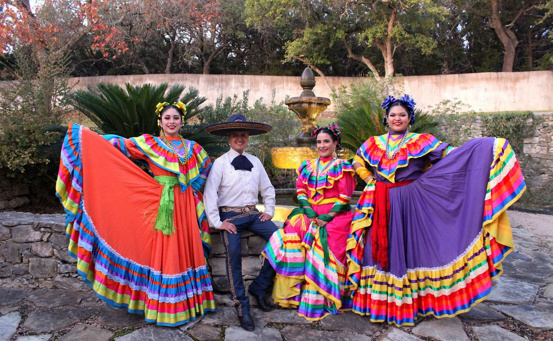 Four members of Grupo Folklórico de Bendiciones wearing colorful traditional costumes by a fountain